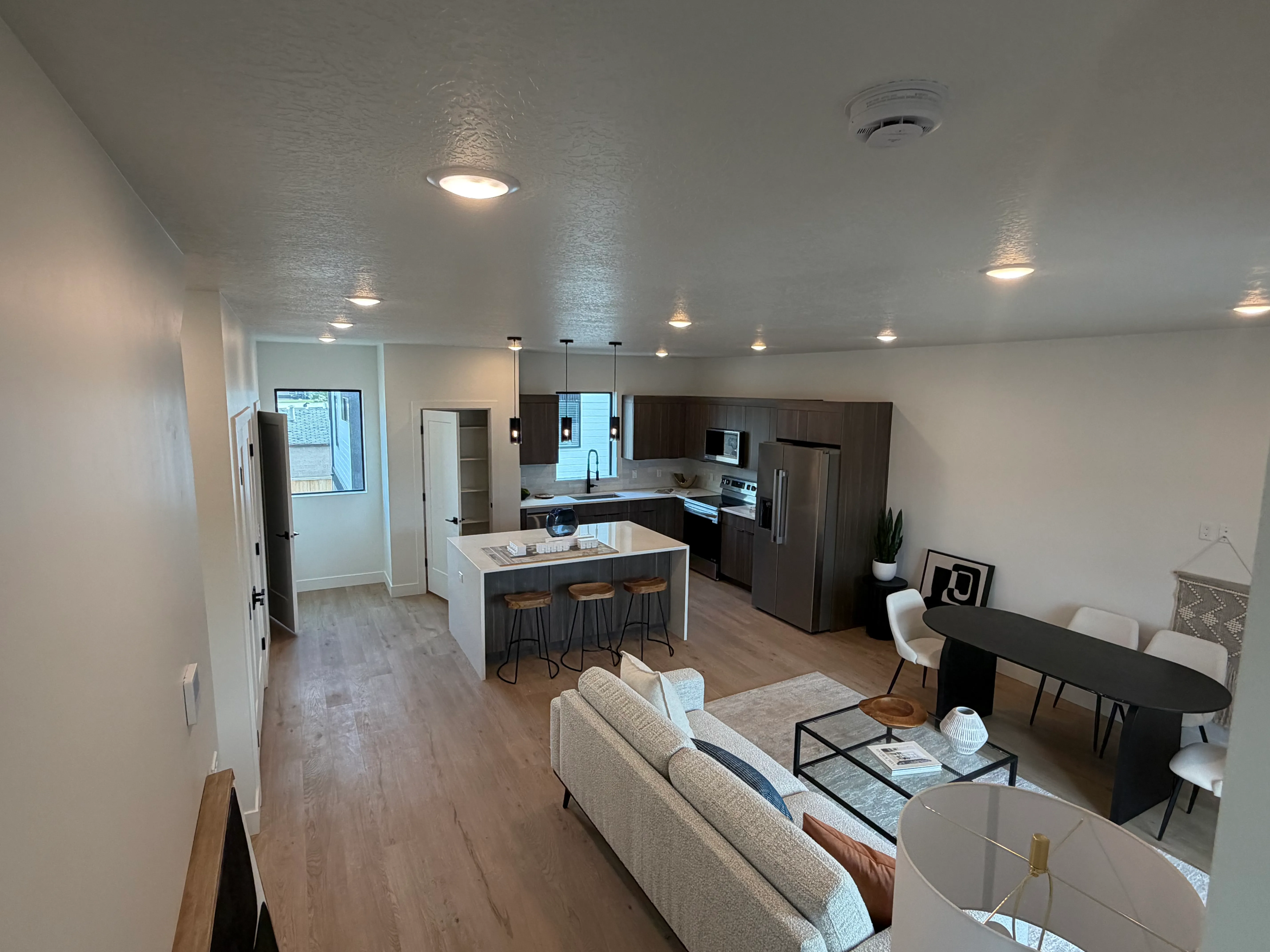Open-concept layout from the living area toward the kitchen, staged with a sofa, dining table, and breakfast-bar seating