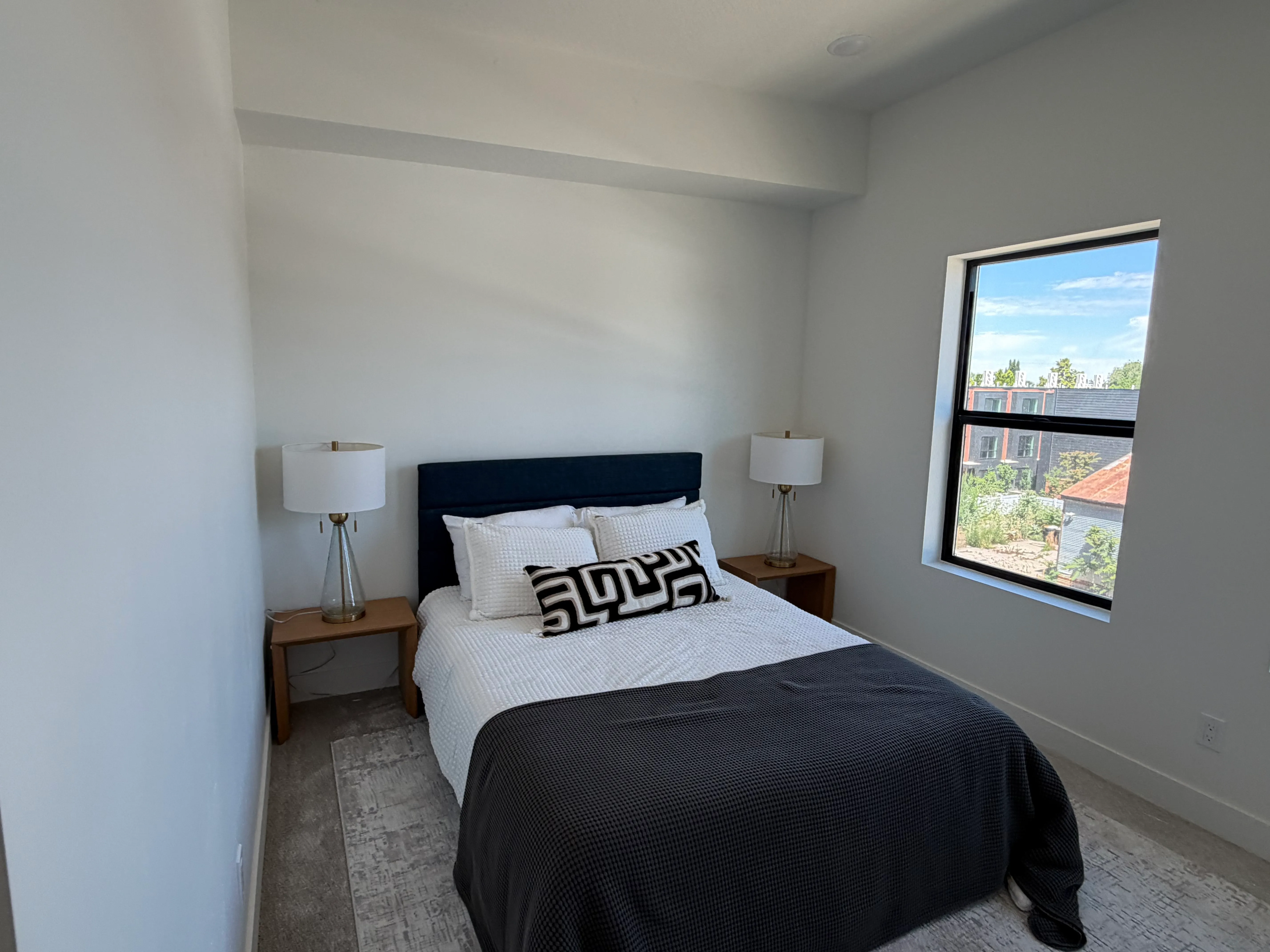 Primary bedroom staged with a queen bed, matching nightstands and lamps, and a bright window