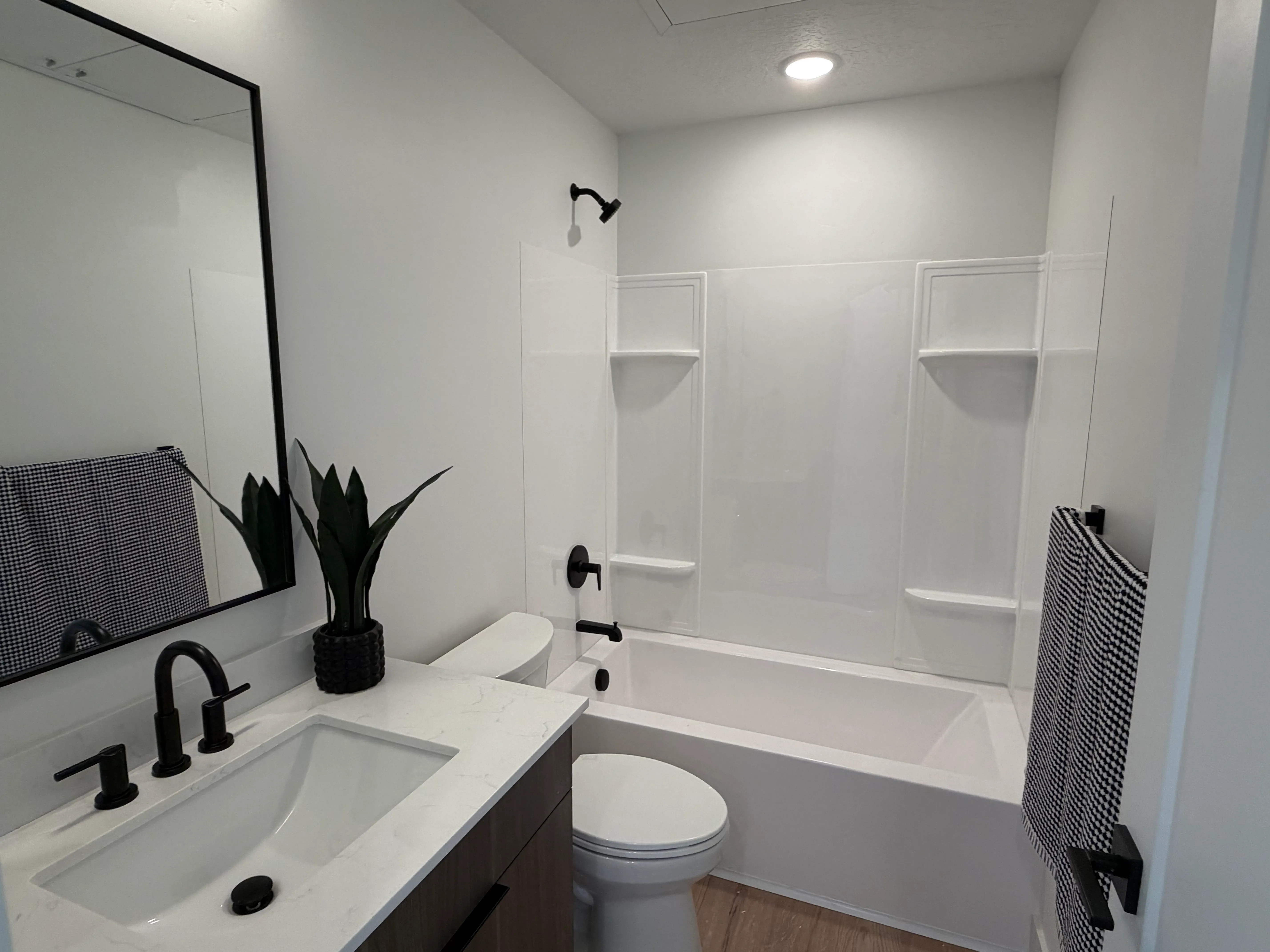 Full bathroom with a soaking tub and shower, matte-black fixtures, a quartz-topped vanity, and styled towels and greenery